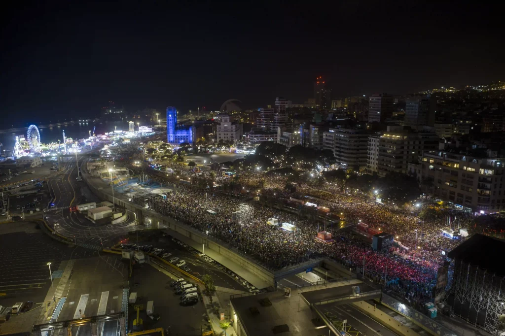Fête nocturne animée du Carnaval de Tenerife à la Plaza de España avec des lumières de scène, des costumes colorés et des milliers de personnes.