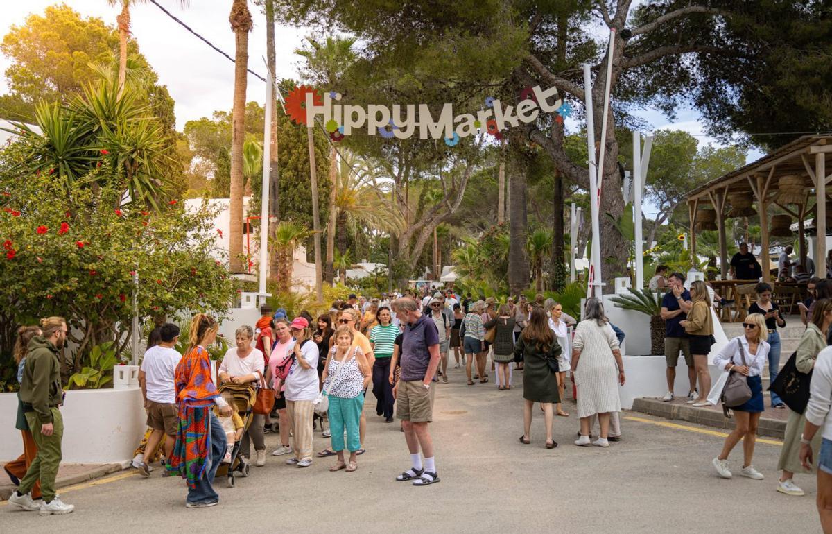 Daytime entrance to the Hippy Market: a colorful letter sign hanging between trees and palm trees, with people strolling down the street